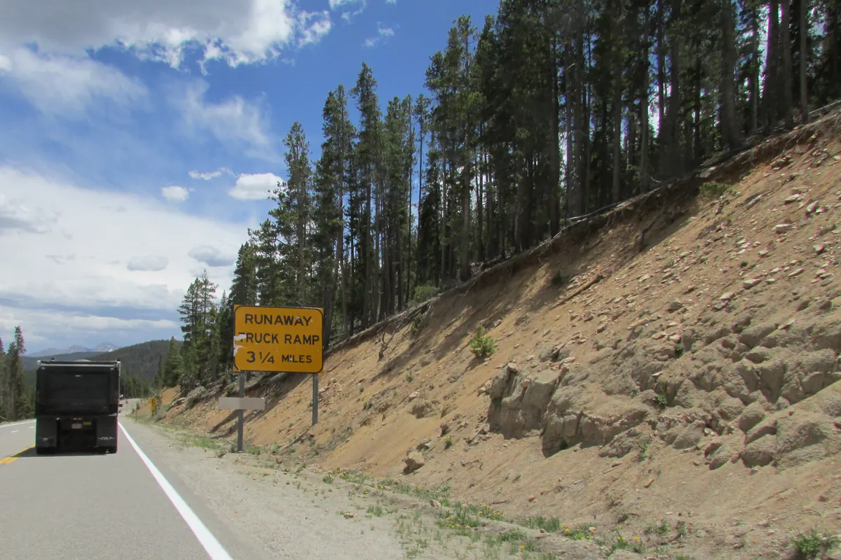Dump truck ahead on a mountain highway grade, with a yellow runaway truck ramp sign and a steep roadside slope