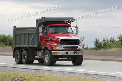 Red tandem-axle dump truck driving on a highway