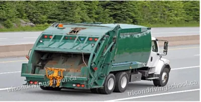 Green rear-loader garbage truck seen from behind on a highway