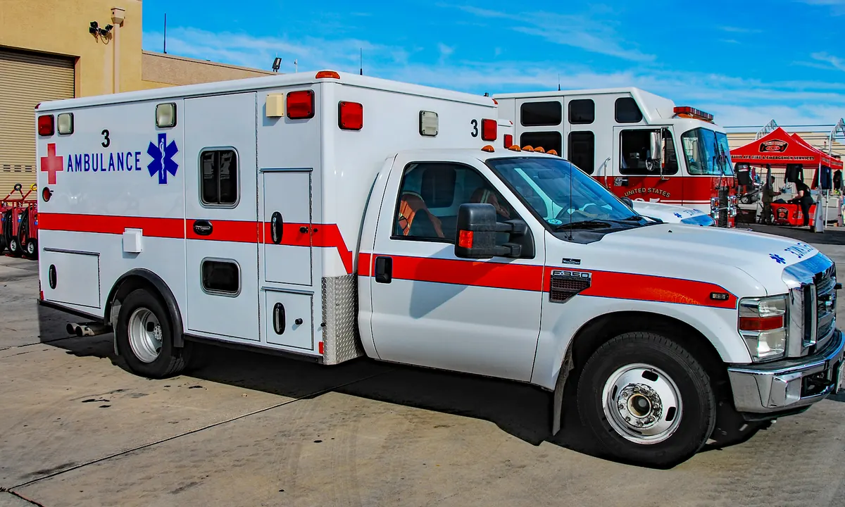 White ambulance with a red stripe, a red cross and the word AMBULANCE on the side, parked outdoors